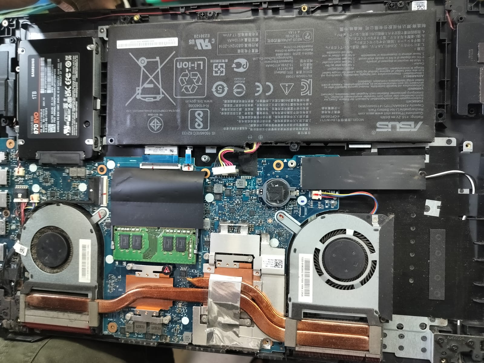 ASUS laptop opened to show battery, SSD, RAM, and cooling assembly